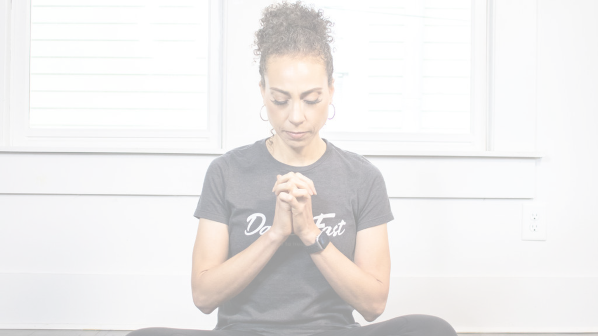 middle aged woman in dark grey t-shirt sitting with head bowed and praying